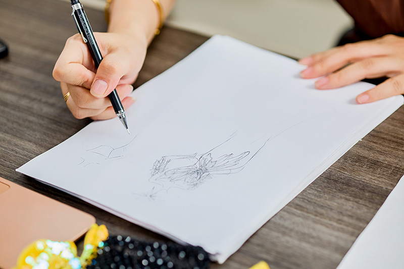机に置かれた、デザイナーの手描きオートクチュールのスケッチとビーズ加工の材料